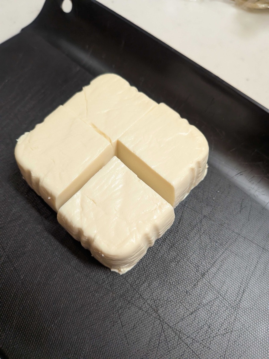 Firm tofu cut into four equal pieces on a black cutting board