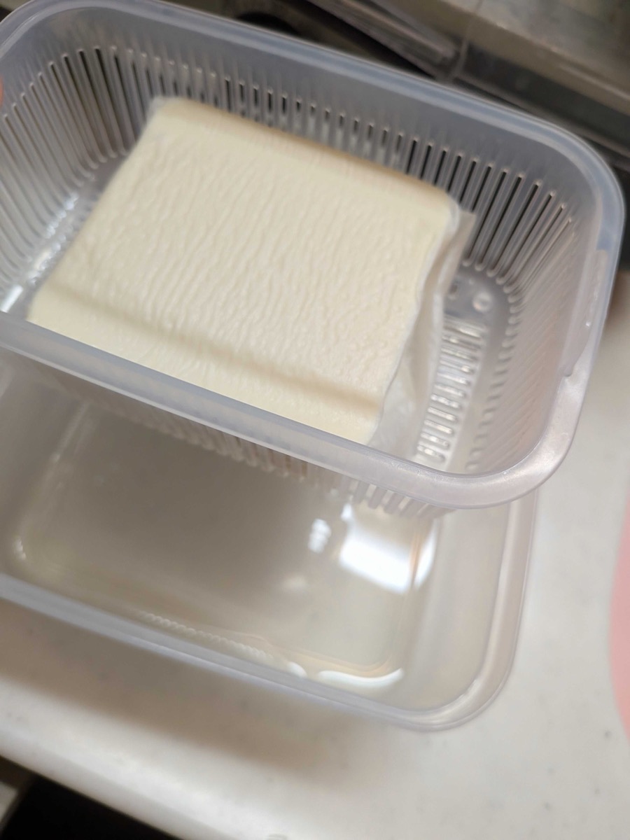 Firm tofu draining in a plastic strainer container
