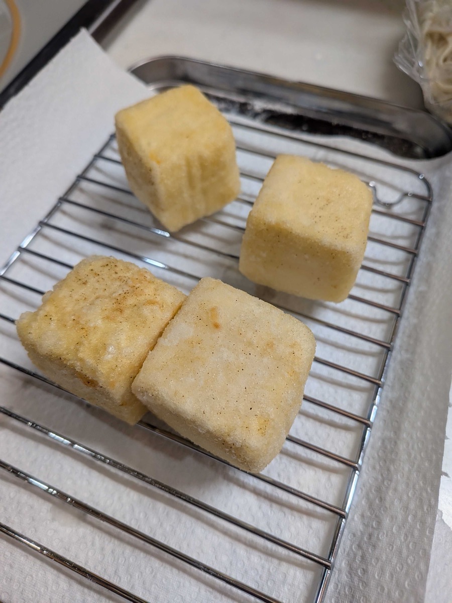 Fried tofu pieces draining on a wire rack over paper towels