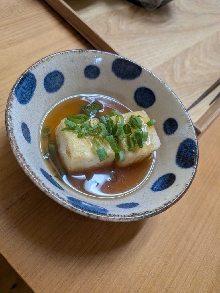 Agedashi tofu served in a blue dotted ceramic bowl with dashi broth and sliced green onions on top