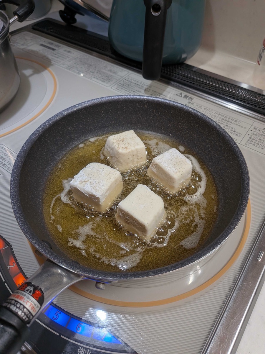 Tofu pieces frying in oil in a pan over medium-high heat