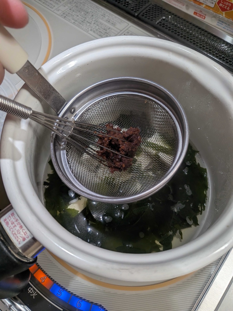 Miso paste being dissolved through a strainer into dashi broth