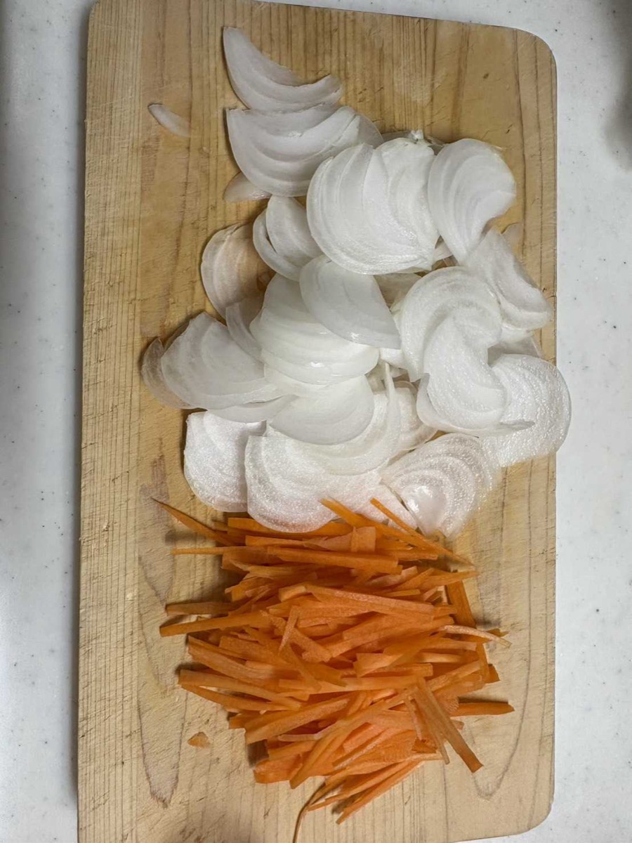 Sliced onion and julienned carrot on a wooden cutting board