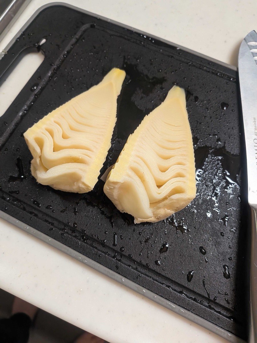 Boiled bamboo shoot cut in half showing pale yellow interior on a cutting board