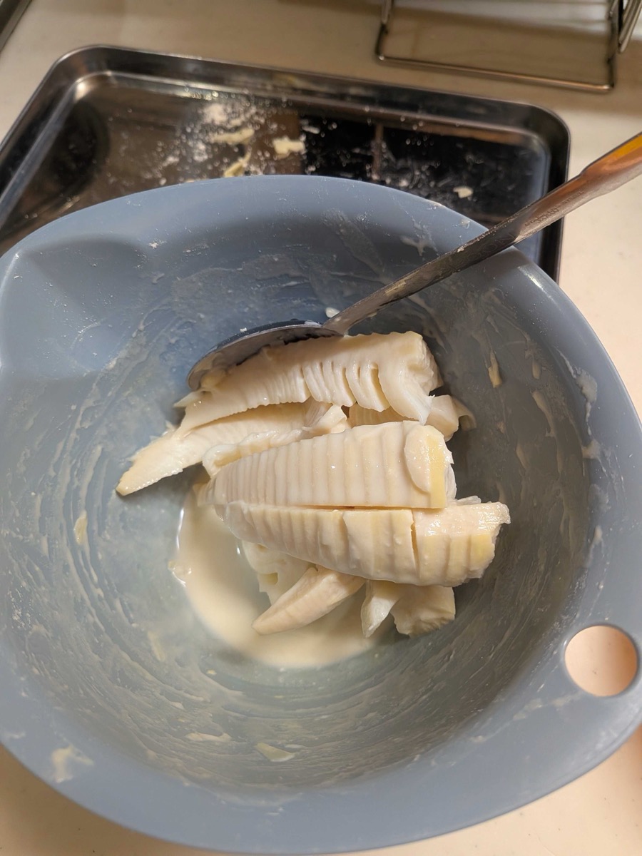 Bamboo shoot slices being coated in tempura batter in a bowl