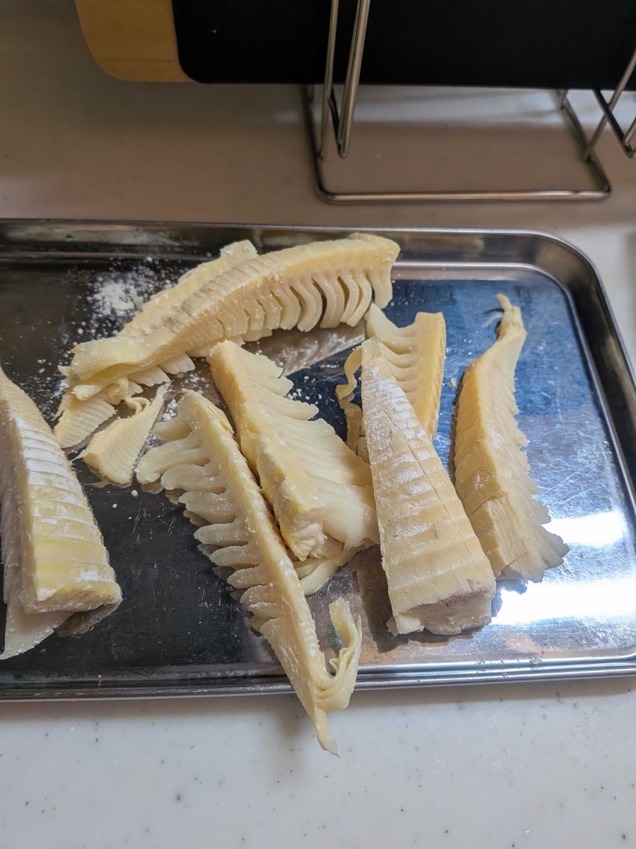 Sliced bamboo shoots dusted with flour on a metal tray ready for battering