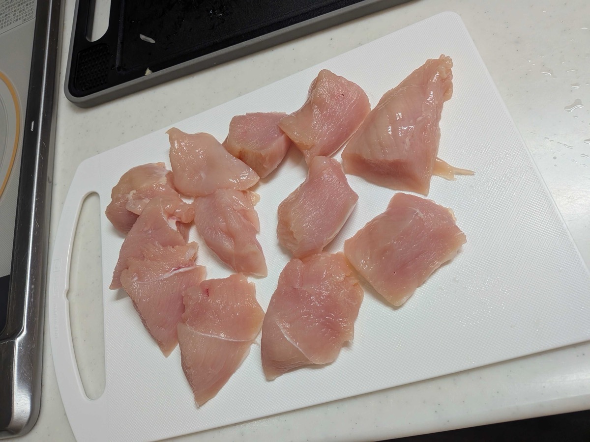Chicken breast cut into bite-sized pieces on a white cutting board