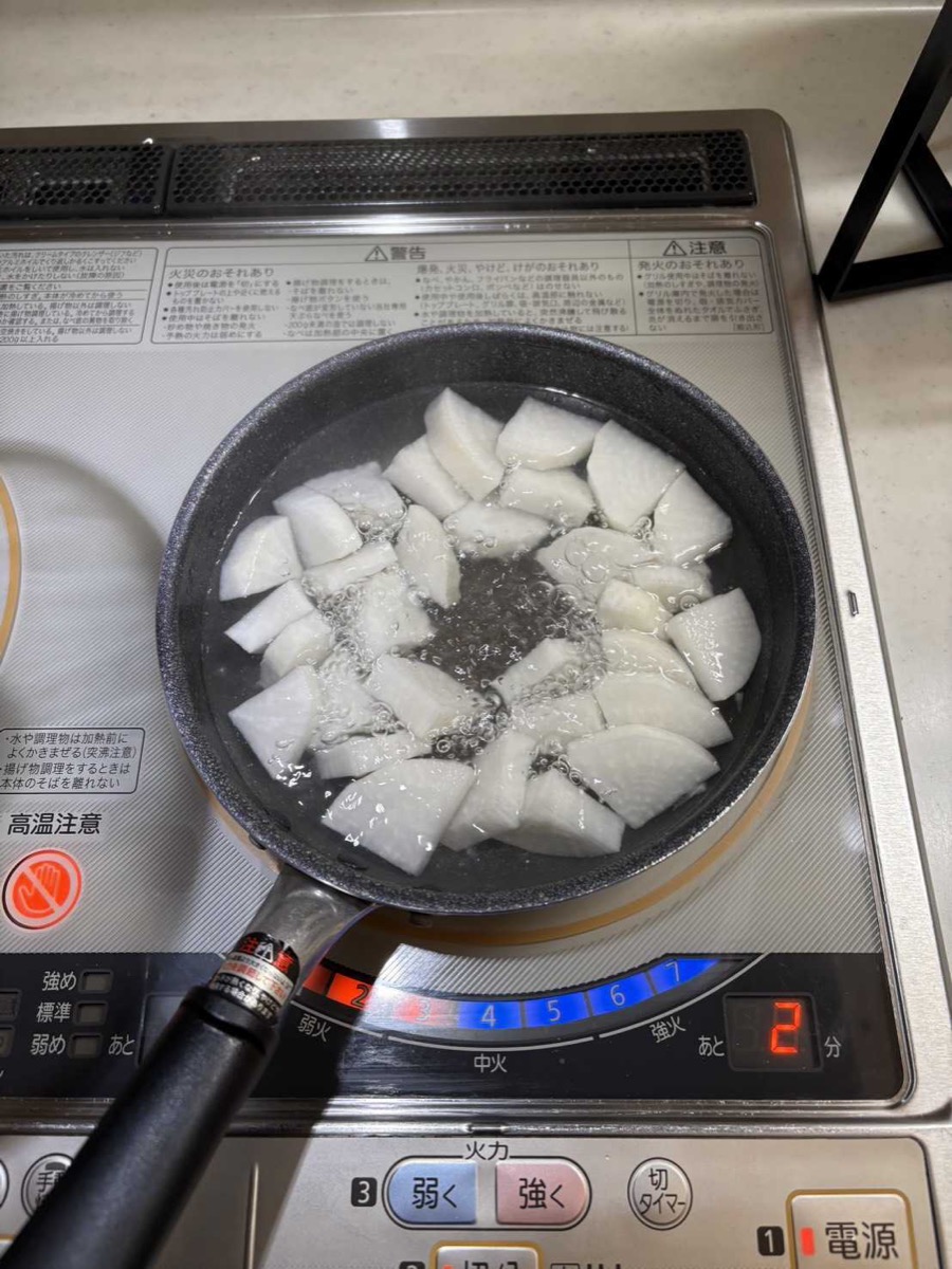 Daikon pieces blanching in a pan of boiling water on an IH cooktop
