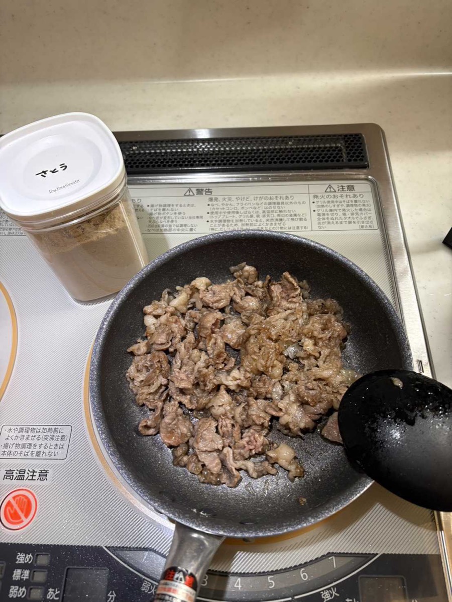 Thinly sliced beef brisket being sautéed in a dark frying pan on an IH cooktop