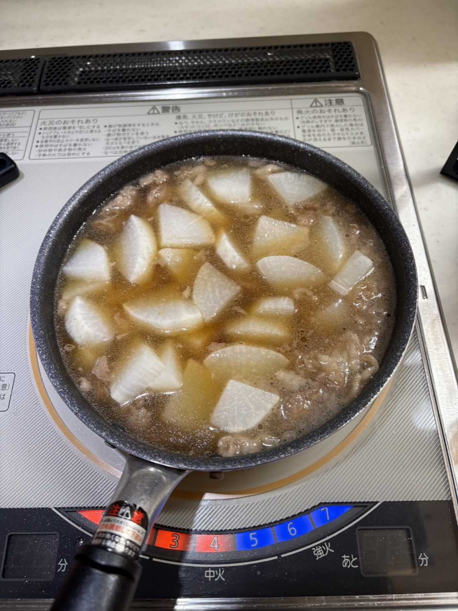 Daikon and beef simmering together in seasoned dashi broth in a pan, viewed from above