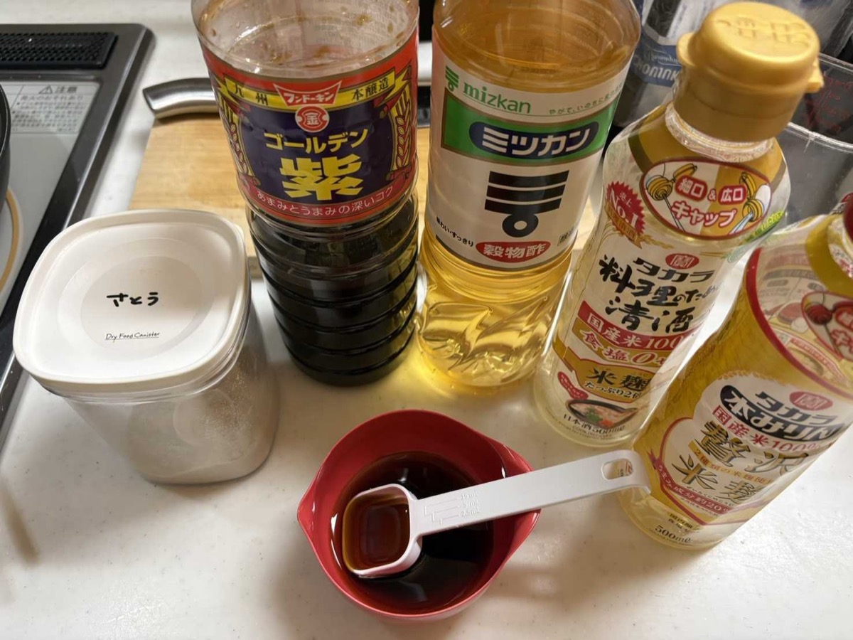 The premixed sweet-and-sour sauce for buta amazu itame in a small red bowl with a measuring spoon, surrounded by the soy sauce and vinegar bottles