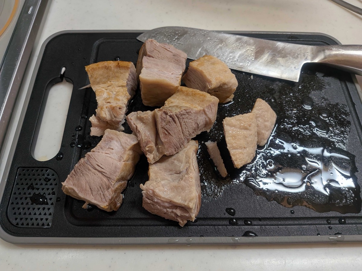 The pre-boiled pork belly cut into roughly 4cm cubes on a black cutting board, showing the pale, tender meat ready for braising