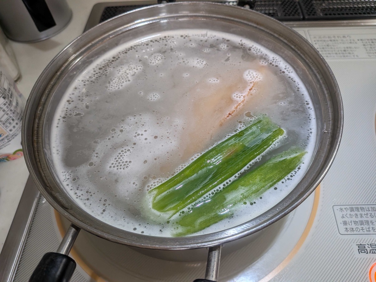 The pork belly continuing to simmer in the milky rice water with a stalk of green scallion added — a traditional Japanese aromatic for kakuni