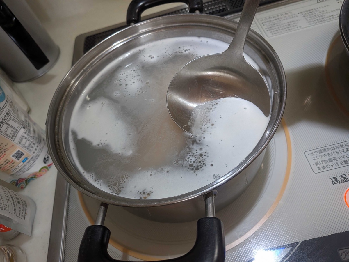 A pot of milky-coloured water pre-boiling the pork belly with uncooked rice — the traditional Japanese technique for rendering fat and tenderising the meat for kakuni