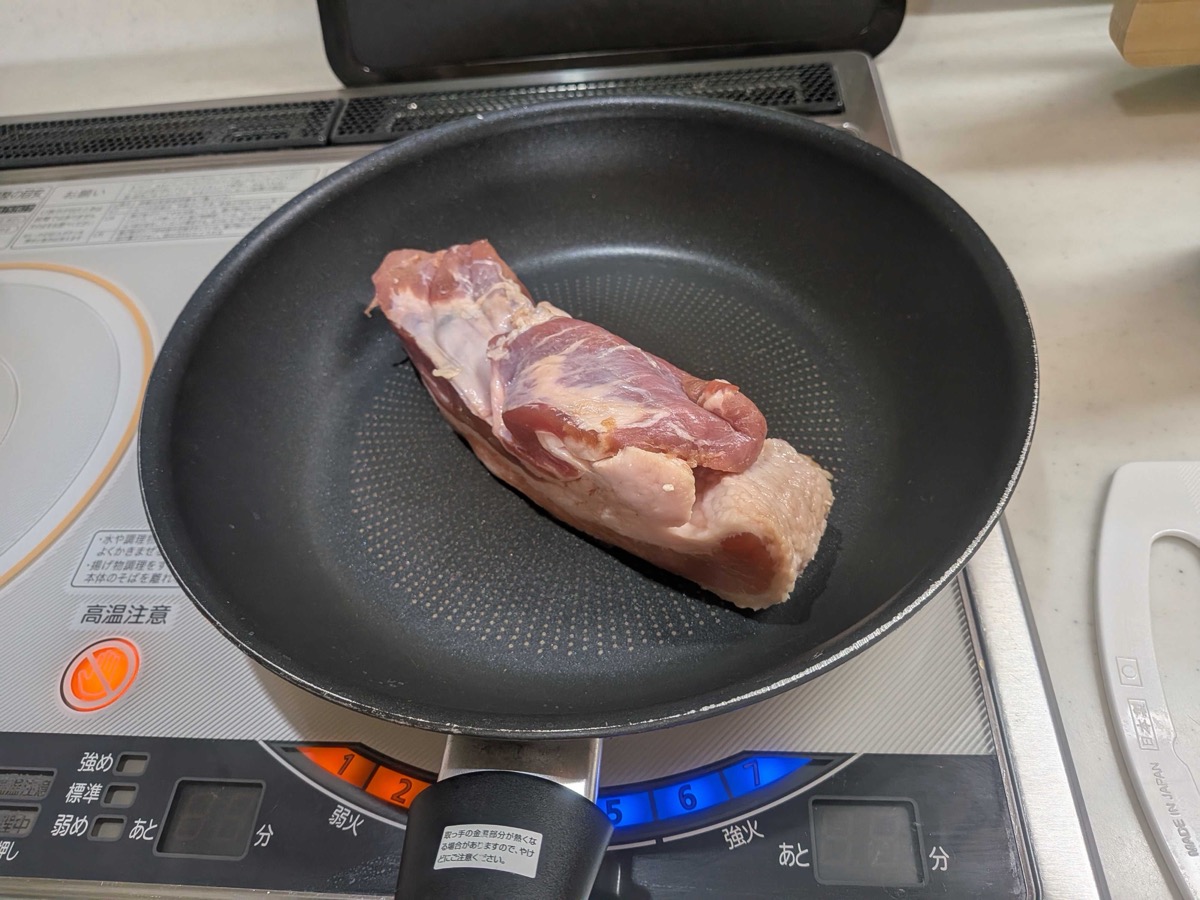 A whole pork belly block placed fat-side down in a black frying pan on an IH cooktop, just starting to sear