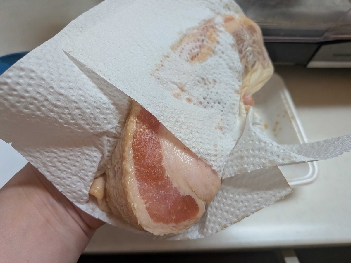 A block of pork belly being patted completely dry with paper towels after the soy sauce rub — an essential step before searing for Japanese kakuni