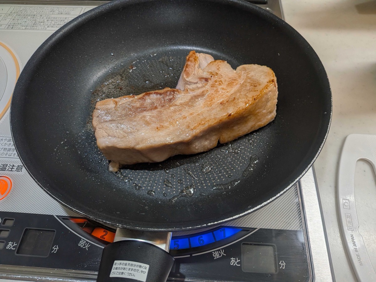 The pork belly block fully seared golden brown on all sides in a frying pan, ready to be transferred to the pre-boil pot