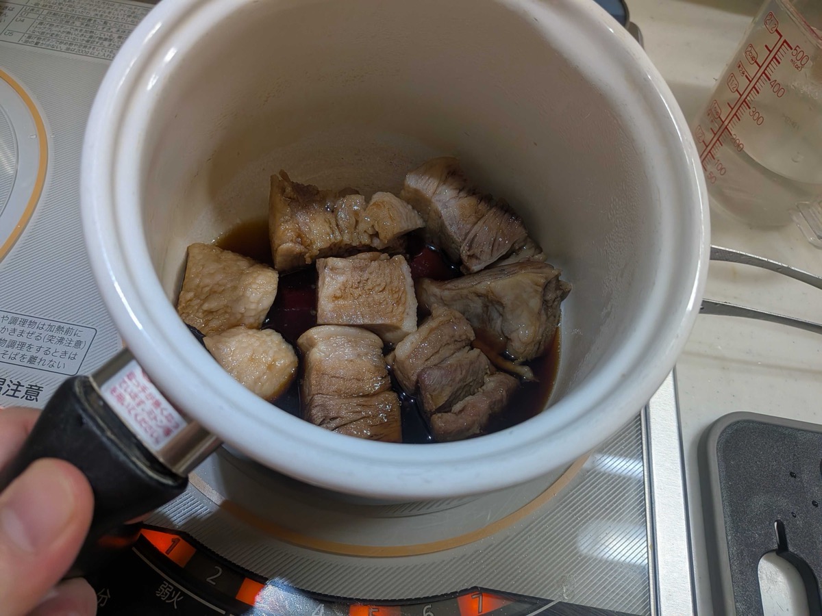 Cubes of pre-boiled pork belly arranged in a small white Japanese braising pot with dark soy-and-sake glaze coating the meat