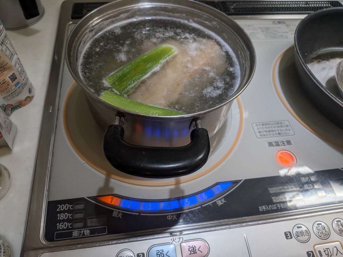 The pork belly simmering vigorously in the rice water with the scallion green — about 60 minutes total of pre-boiling for Japanese kakuni