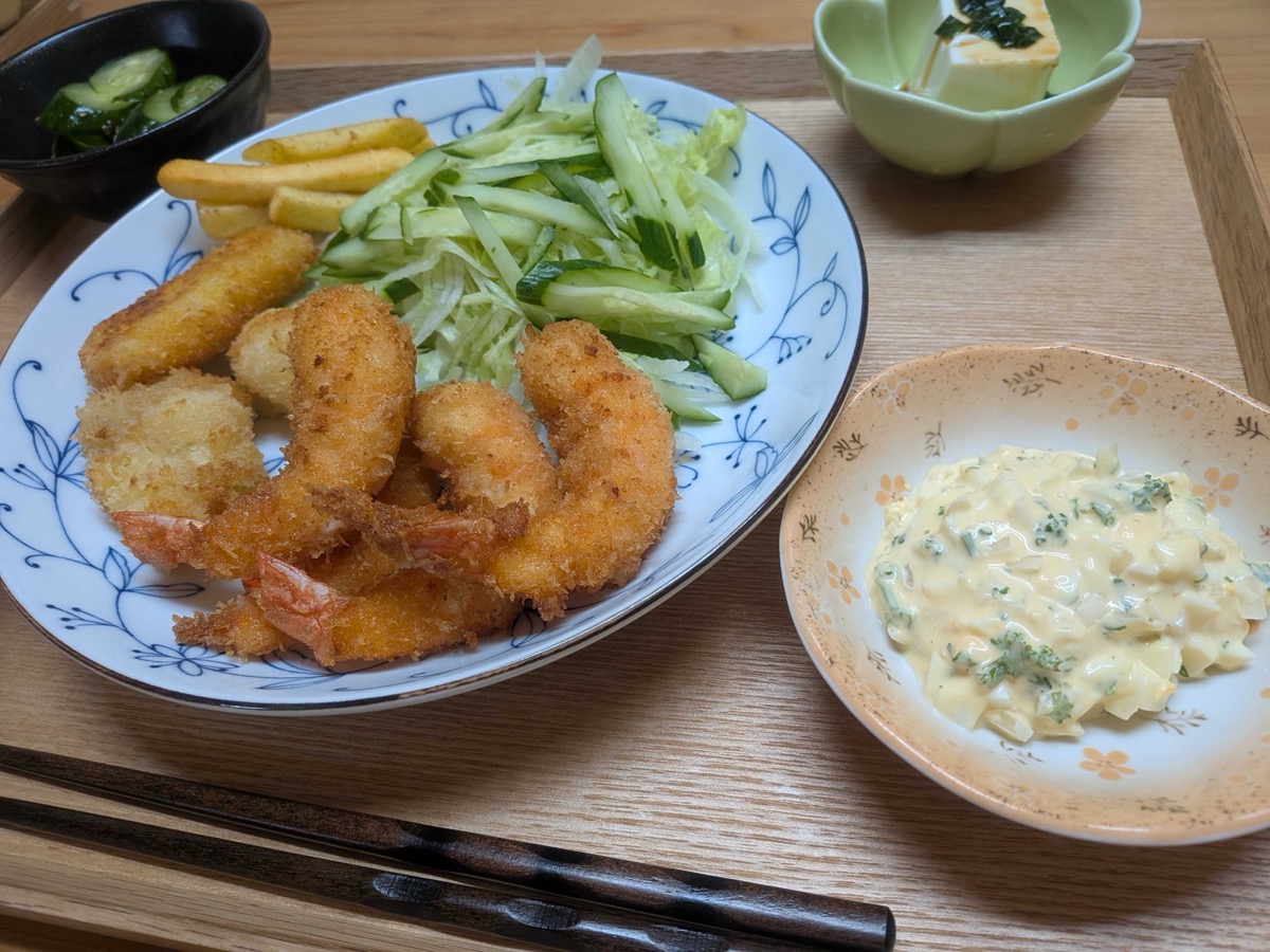 A finished plate of Japanese ebi fry — golden panko-fried shrimp served on a blue and white plate with shredded cabbage, cucumber, and a generous side dish of homemade tartar sauce on a wooden tray