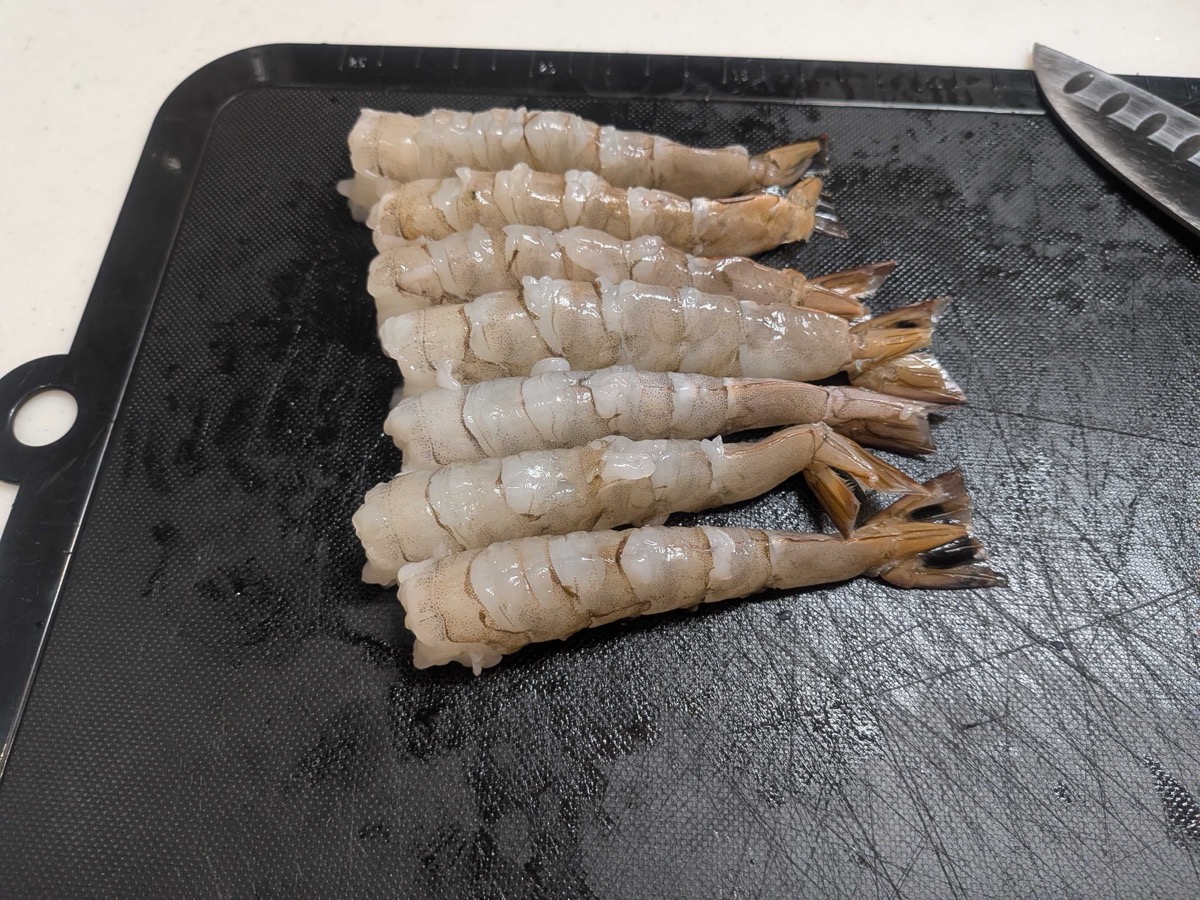 Six peeled and deveined large shrimp with tails on, arranged on a black cutting board ready for the cleaning step