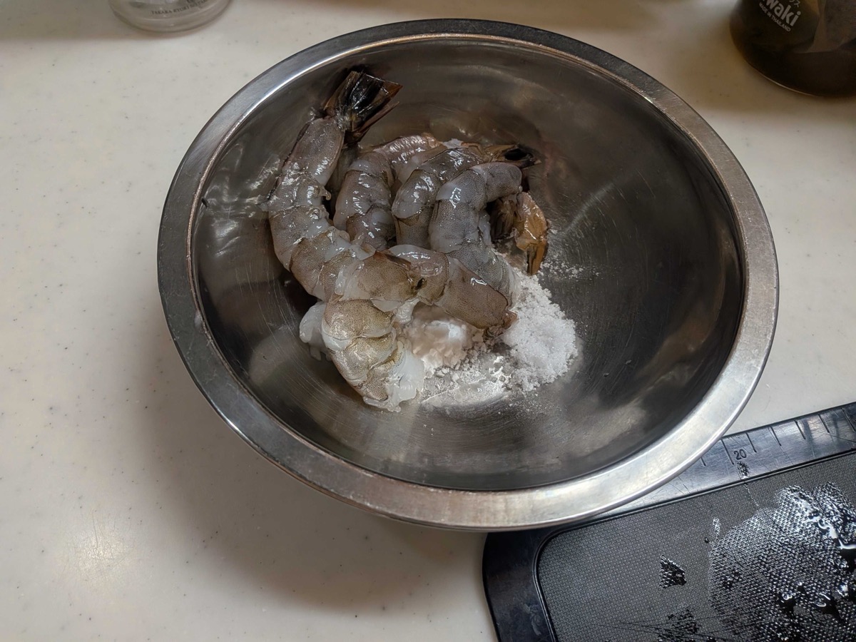 Peeled shrimp in a stainless steel bowl with potato starch and salt for the Japanese cleaning method, just starting to massage