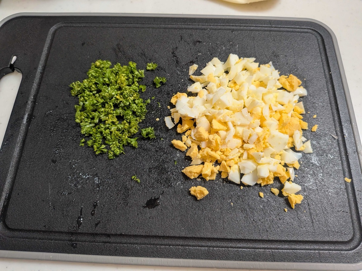 Finely chopped hard-boiled egg and minced fresh parsley on a black cutting board, ready to mix into the tartar sauce