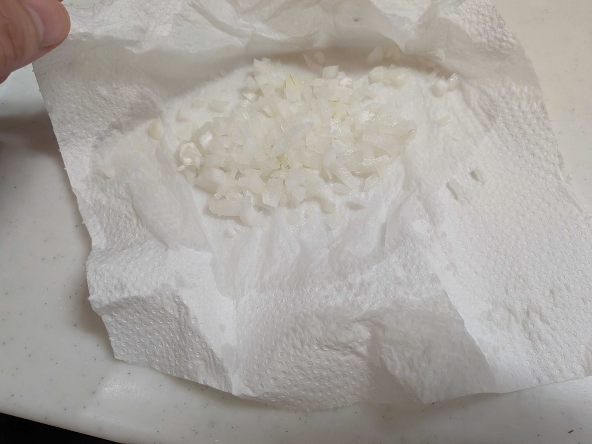 Drained minced onion being pressed dry between sheets of paper towel before going into the tartar sauce