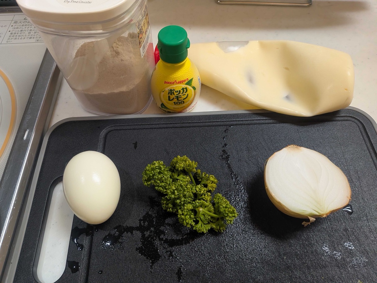 Ingredients for Japanese tartar sauce — a hard-boiled egg, fresh parsley, half an onion, lemon juice, and a sugar container on a kitchen counter