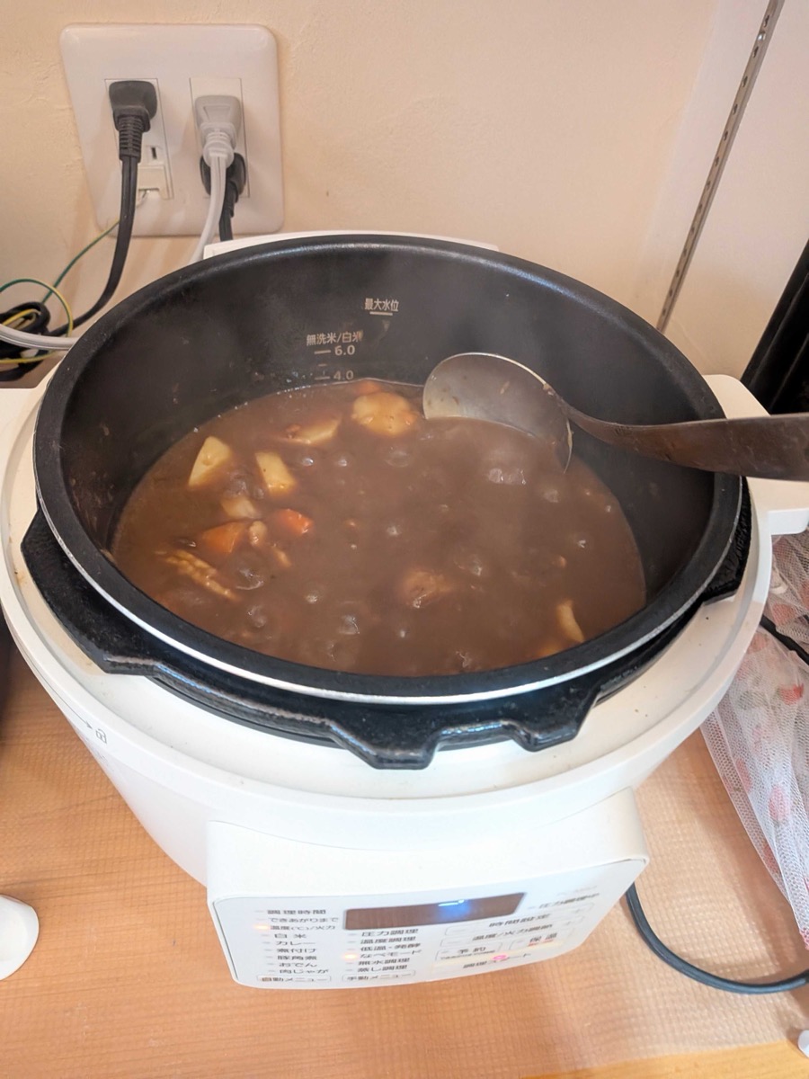 Stirring curry roux into the cooked broth with vegetables and pork in the electric pressure cooker after pressure cooking