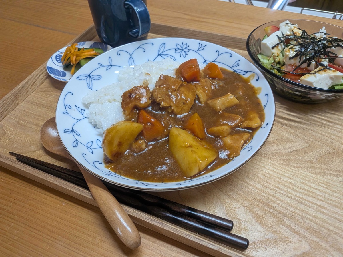 Two breaded tonkatsu cutlets deep frying in hot oil in a black rectangular pan on an IH cooktop, bubbling vigorously