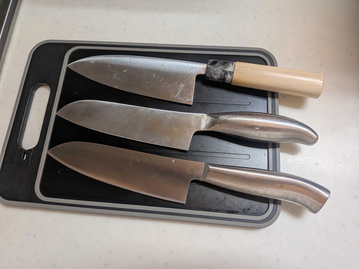 Three Japanese santoku knives of different sizes laid out on a black cutting board — the three-virtues knife is the most popular Japanese all-purpose kitchen knife for meat, fish, and vegetables