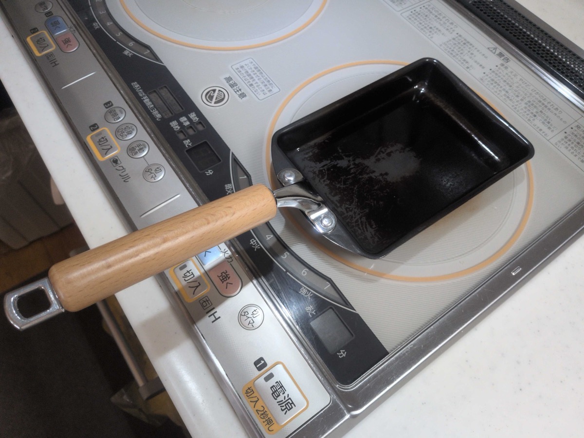 A small rectangular Japanese tamagoyaki pan with a wooden handle, sitting on an IH cooktop — designed specifically for making the Japanese rolled omelette