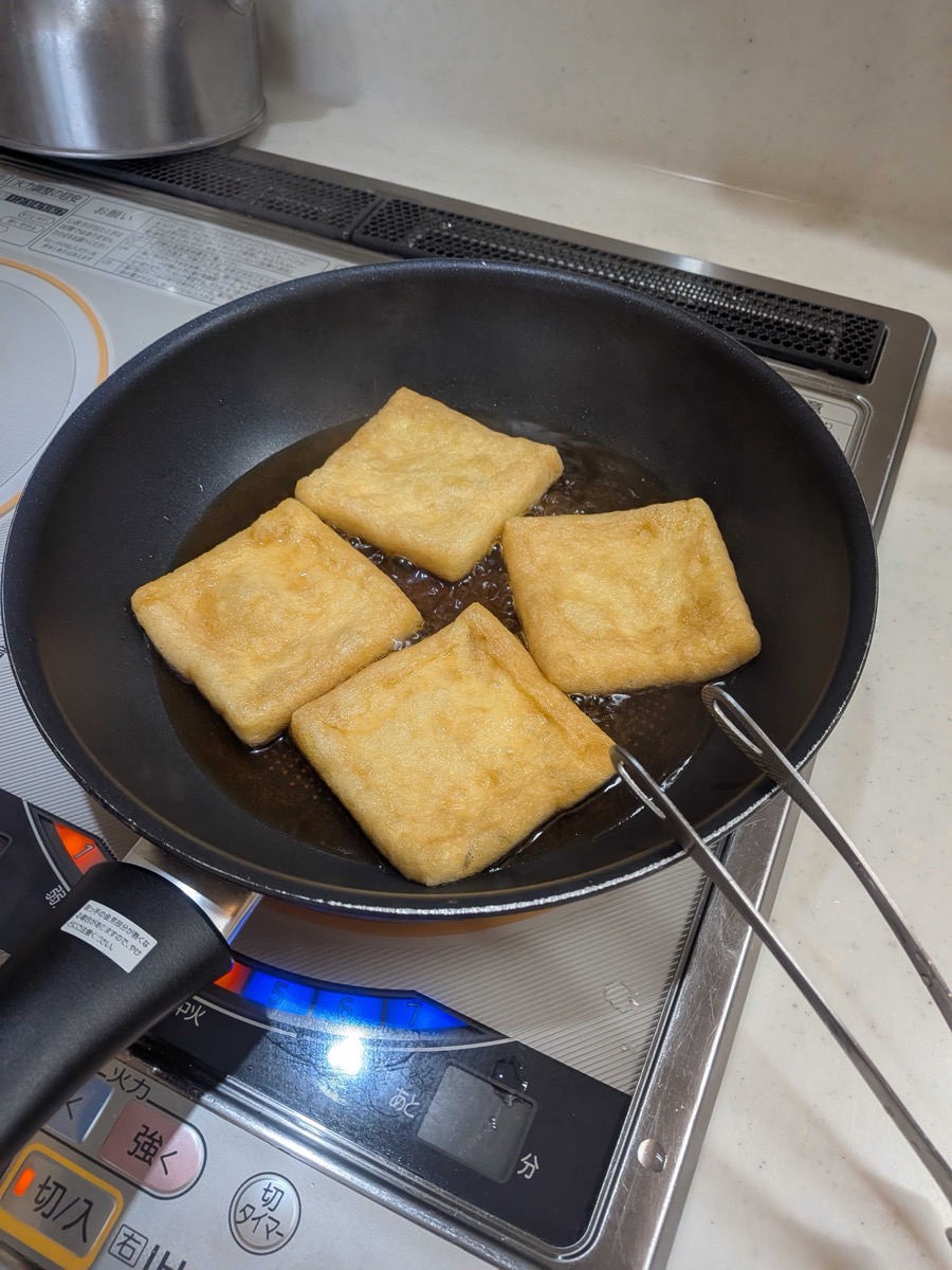 Four golden-amber aburaage tofu pouches finished simmering in the sweet-savoury broth, deep in colour and ready to rest