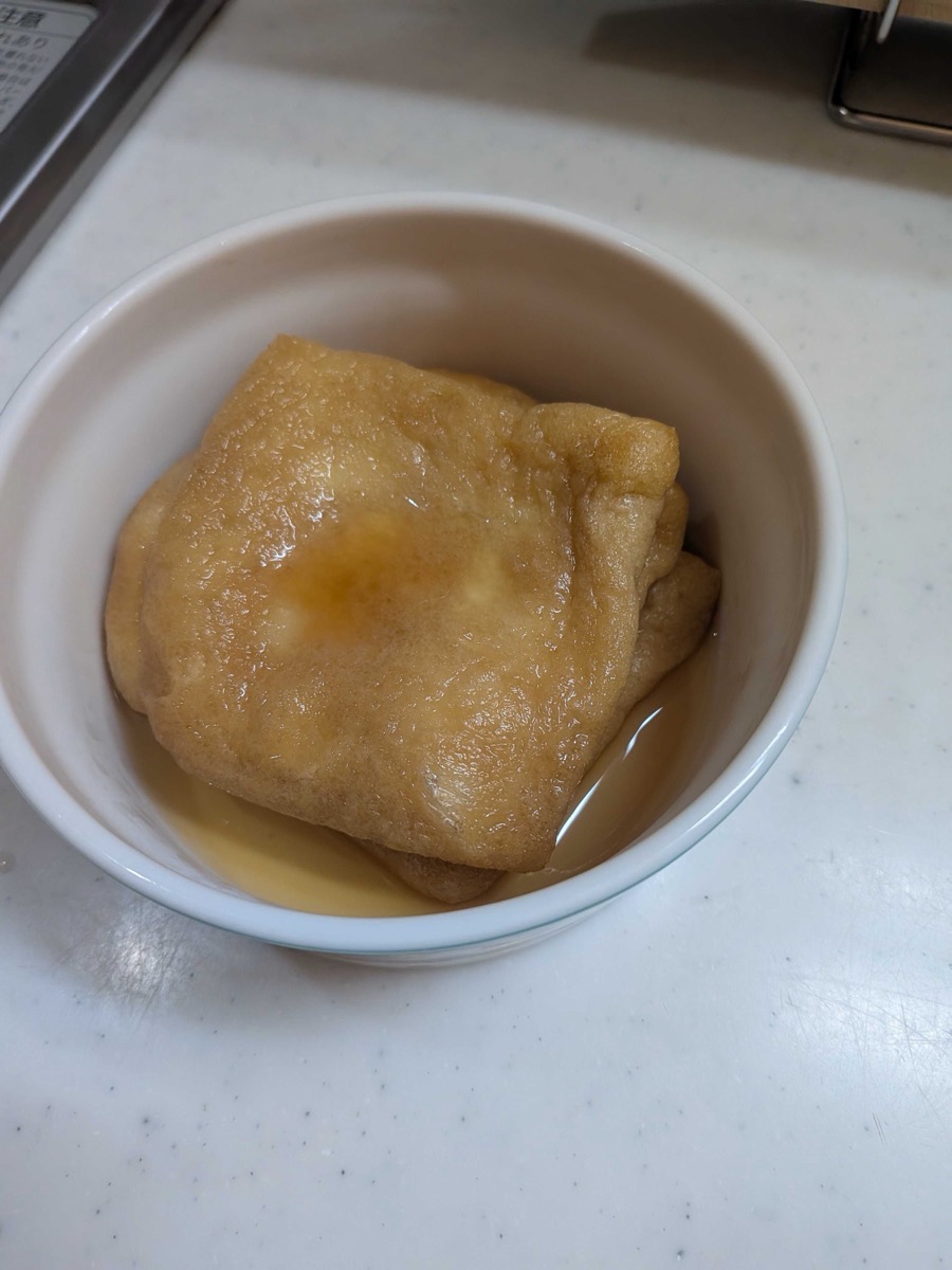 Two sweet simmered aburaage tofu pouches (kitsune udon no age) in a small white bowl with their amber simmering liquid