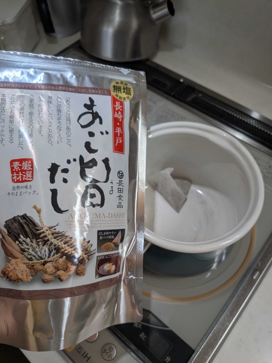 Japanese ago-uma dashi packet by Nagata Foods next to a white pot with a dashi pack steeping in water on an IH cooktop