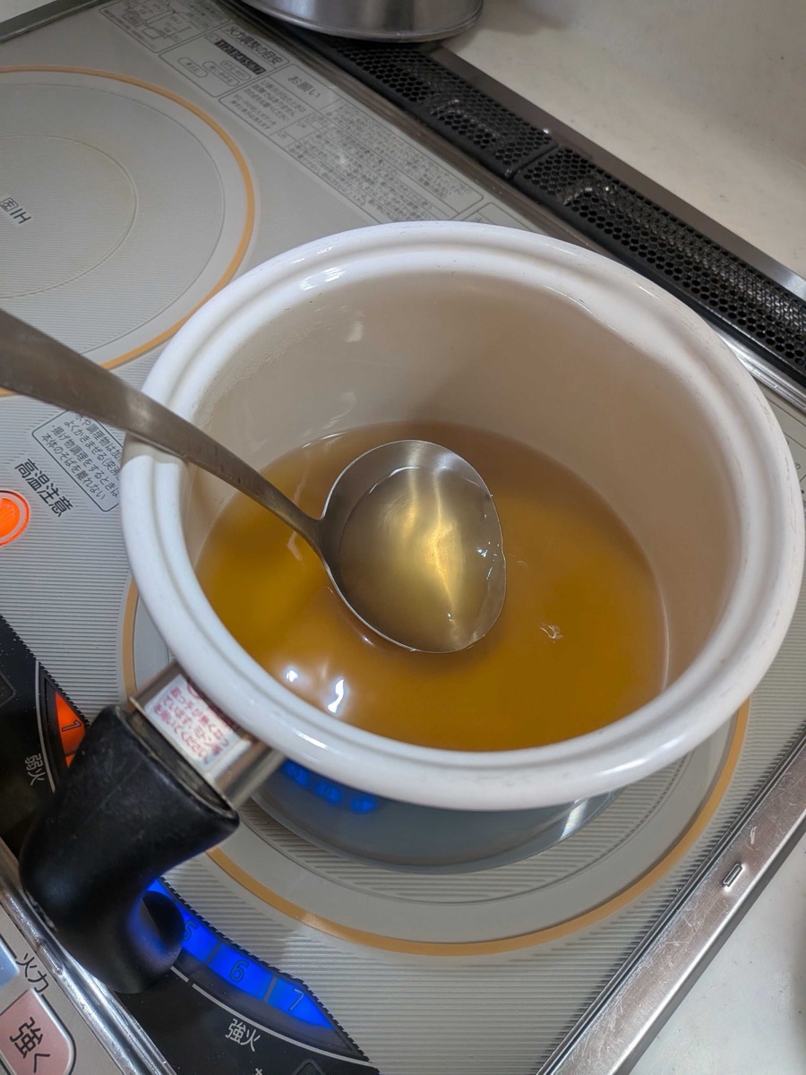 The finished kitsune udon broth — clear golden dashi seasoned with usukuchi soy sauce, in a white pot on an IH cooktop