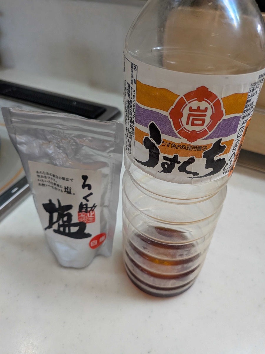 A bottle of usukuchi (light) soy sauce next to a bag of Japanese salt on a kitchen counter — the seasonings used for kitsune udon broth
