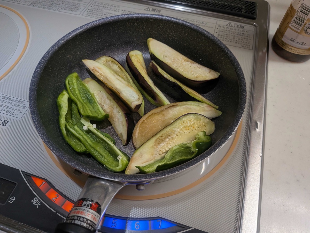Eggplant flipped to its flesh side with green peppers added, all browning together in the frying pan on an IH cooktop