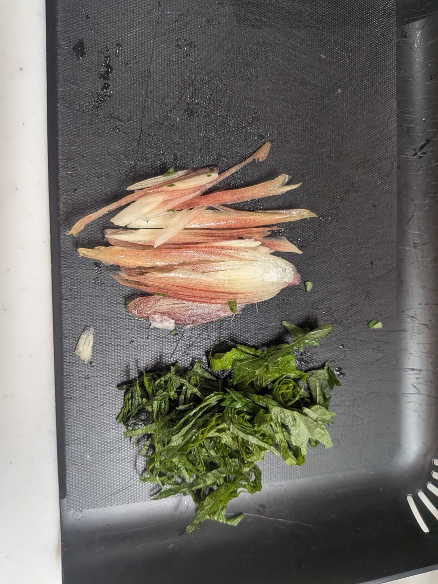 Thinly shredded shiso leaves and slivered myoga arranged separately on a black cutting board, ready to top the yakibitashi