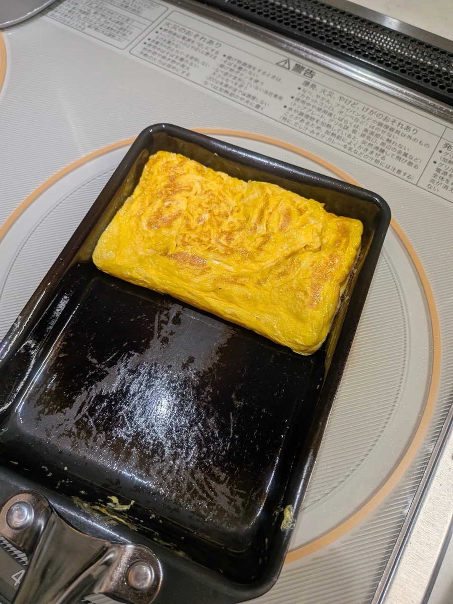 A finished golden tamagoyaki rolled omelette sitting in a rectangular pan, ready to be sliced for spam onigiri