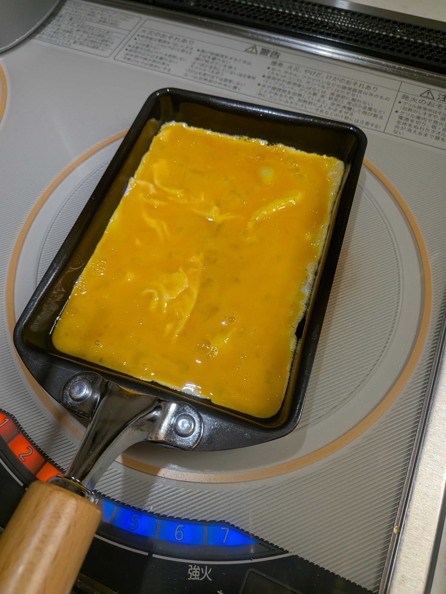 Beaten egg mixture poured into a rectangular tamagoyaki pan on an IH cooktop, just starting to set