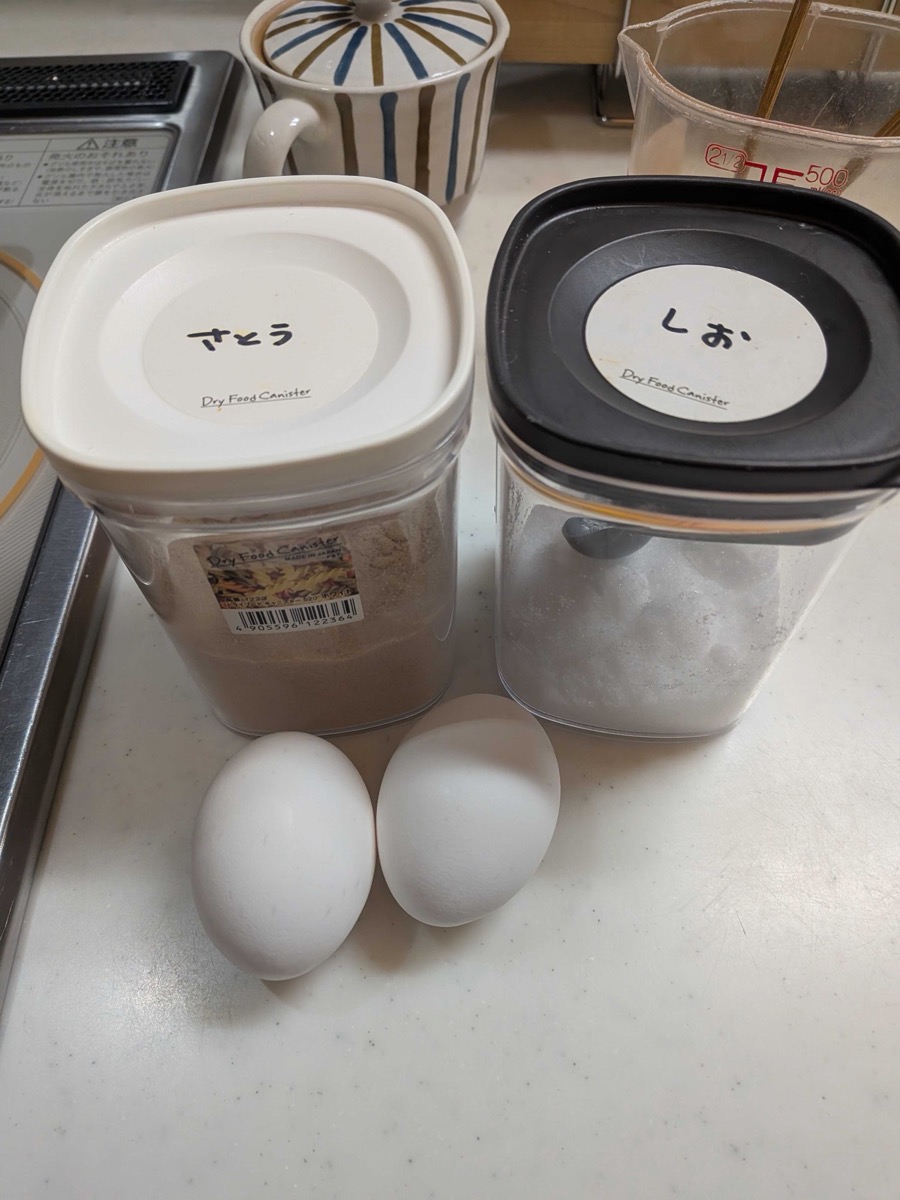 Ingredients for the tamagoyaki layer of Spam onigiri — two eggs, a canister of sugar, and a canister of salt on a kitchen counter