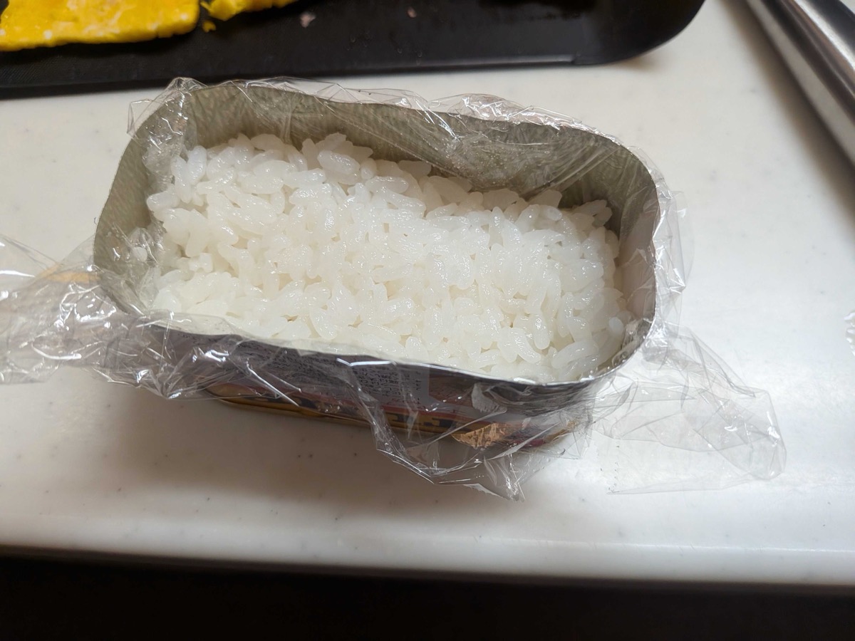 An empty Spam can lined with plastic wrap and packed with cooked Japanese short-grain rice — using the can as a mould for spam onigiri