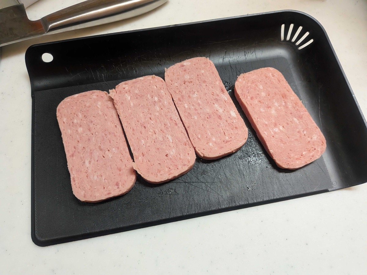 A can of TULIP luncheon meat sliced into four even rectangular pieces on a black cutting board