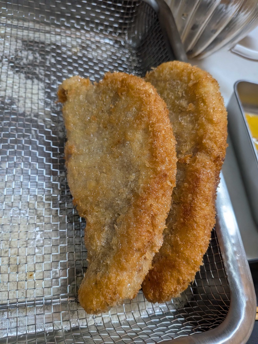 Two golden-brown tonkatsu cutlets draining on a wire rack after deep frying, with a crispy panko crust