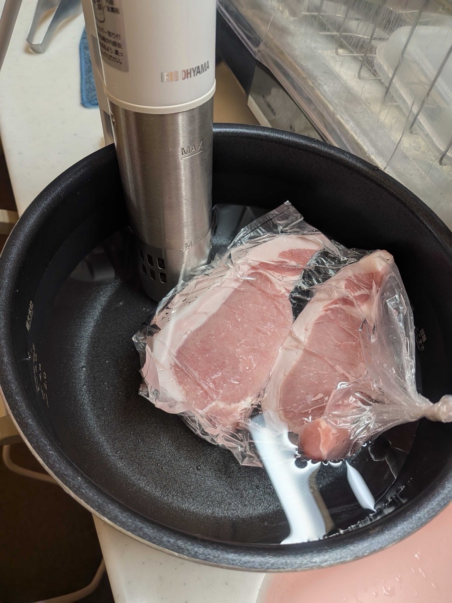 Two pork loin cutlets in vacuum-sealed bags submerged in a sous vide water bath with an immersion circulator