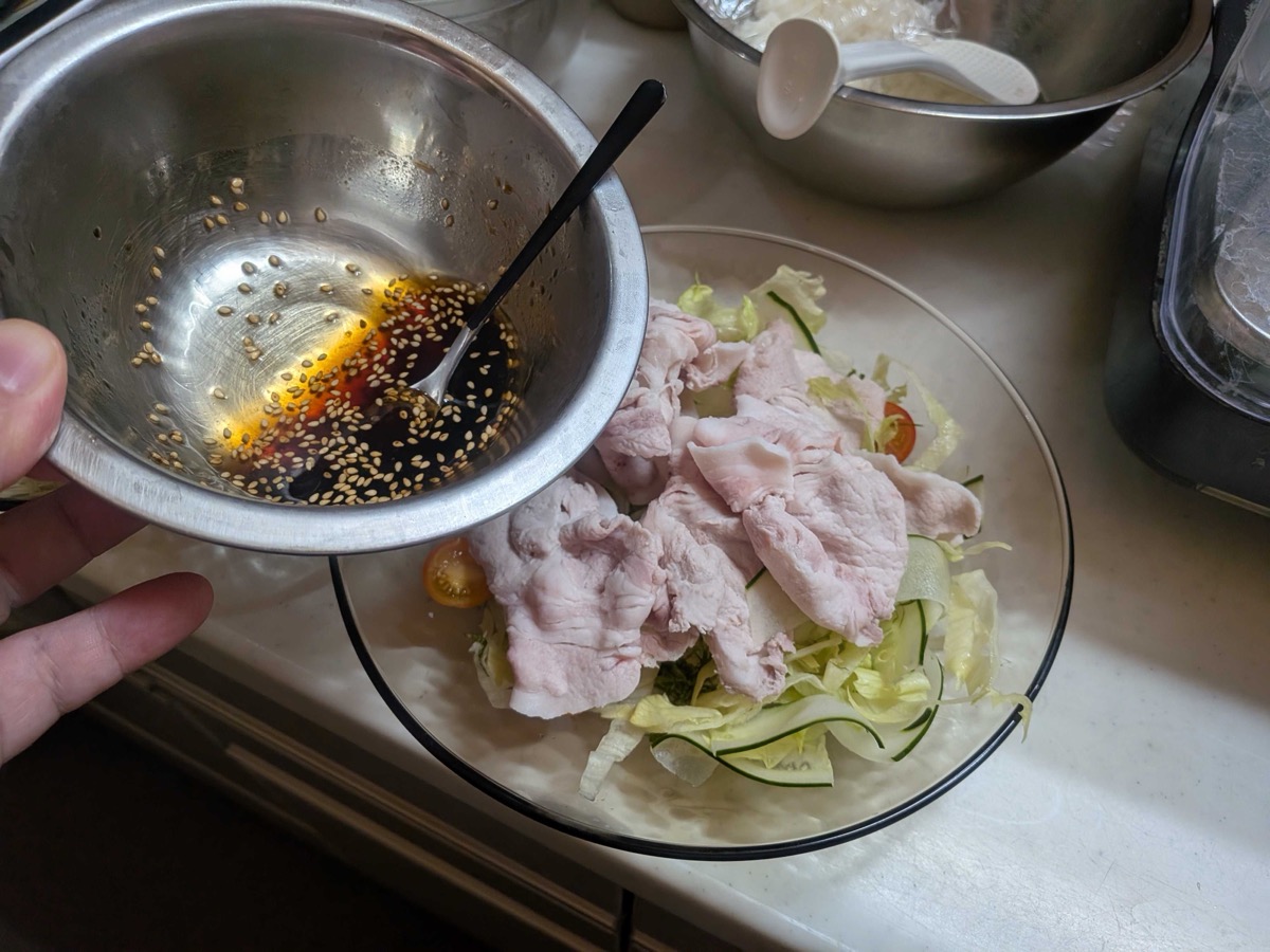 The sesame-soy dressing being spooned over the assembled cold shabu salad