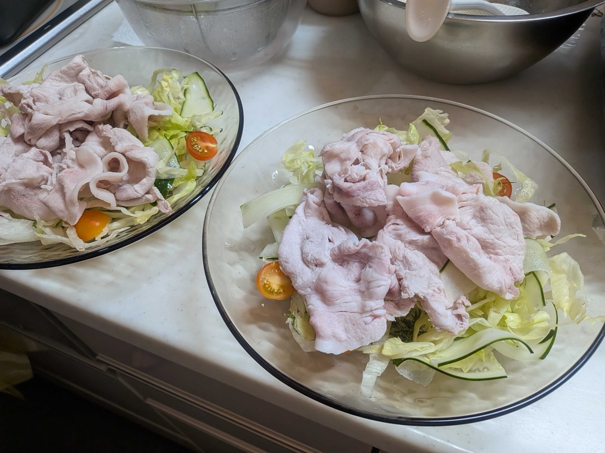 Two plates of shredded lettuce and cucumber topped with cooled poached pork and cherry tomatoes