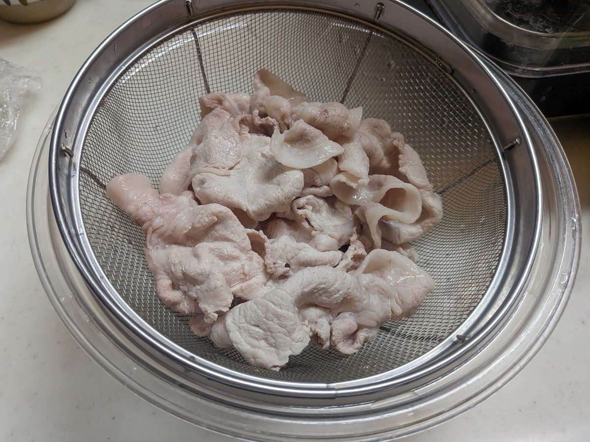 All the poached pork slices drained and cooling in a strainer